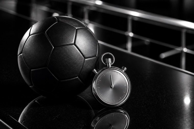 Pallone da calcio e cronometro cromato su un bancone nero lucido in una sala scommesse